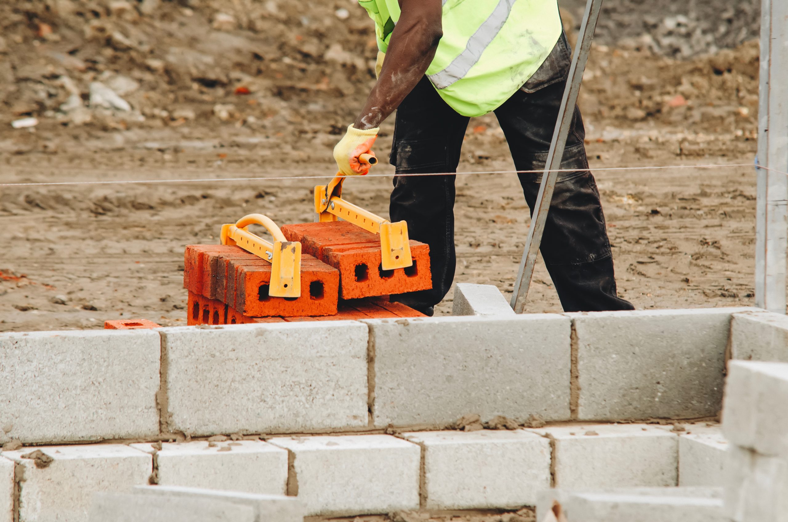 Construction worker manualy lifting bricks on a building site using brick clamp tongs